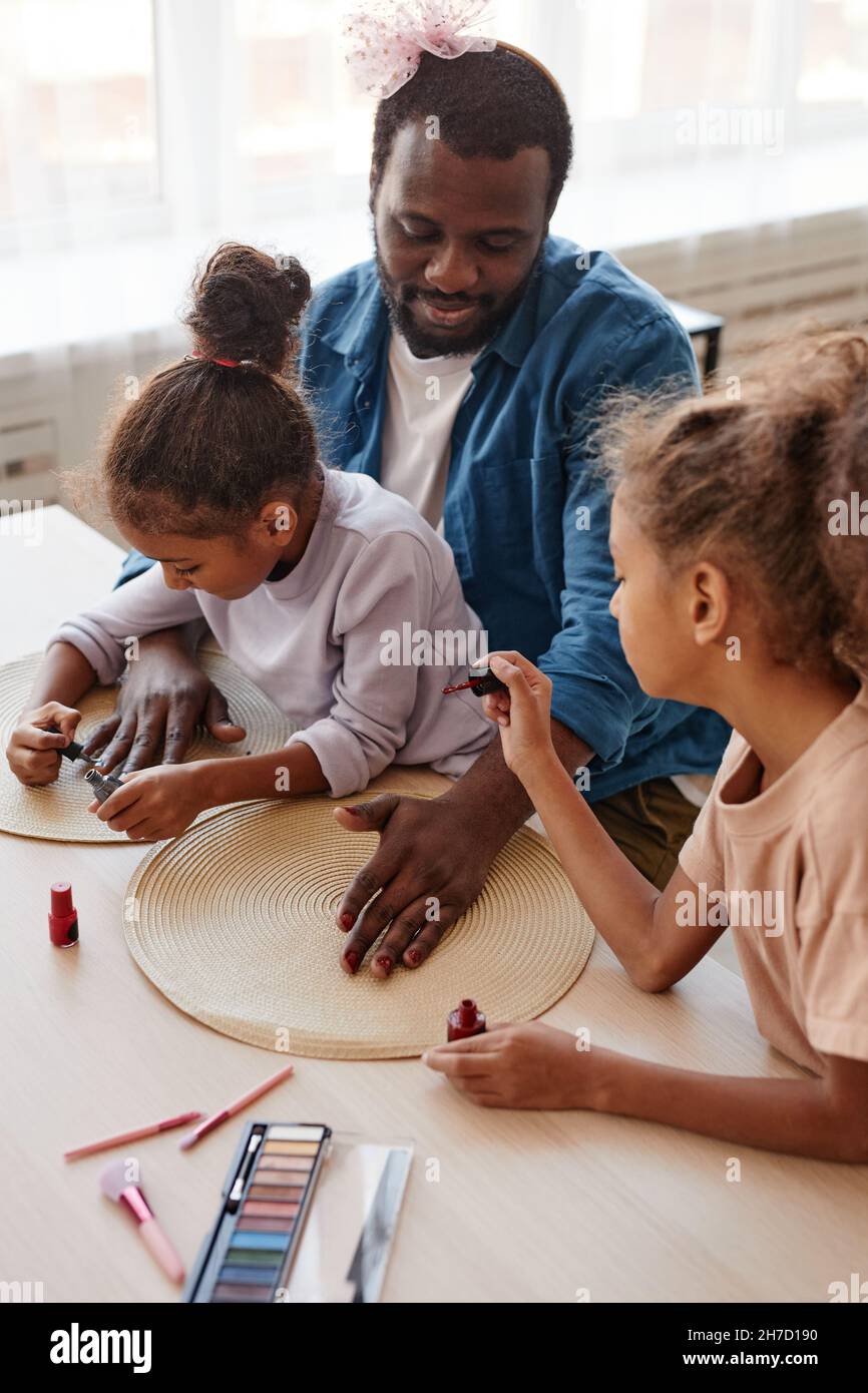 Ritratto verticale di singolo padre afroamericano che gioca con due figlie e che fa il trucco Foto Stock