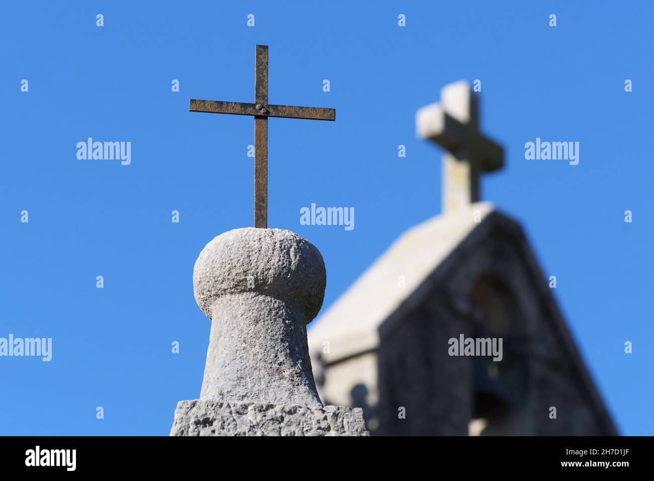 Primo piano di una croce cristiana di ferro arrugginita su un pilastro e campanile della chiesa sullo sfondo. Religione, cristianesimo, architettura e concetti di storia Foto Stock