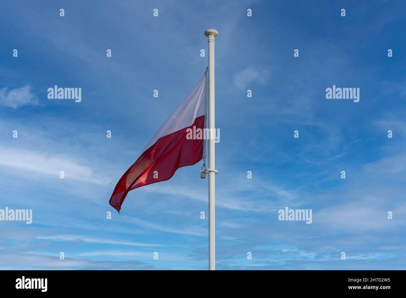 La bandiera nazionale della Polonia vola contro un cielo blu e alcune nuvole bianche. Foto Stock