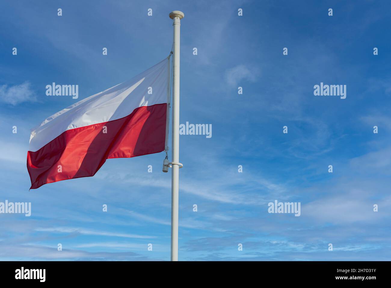 La bandiera nazionale della Polonia vola contro un cielo blu e alcune nuvole bianche. Foto Stock
