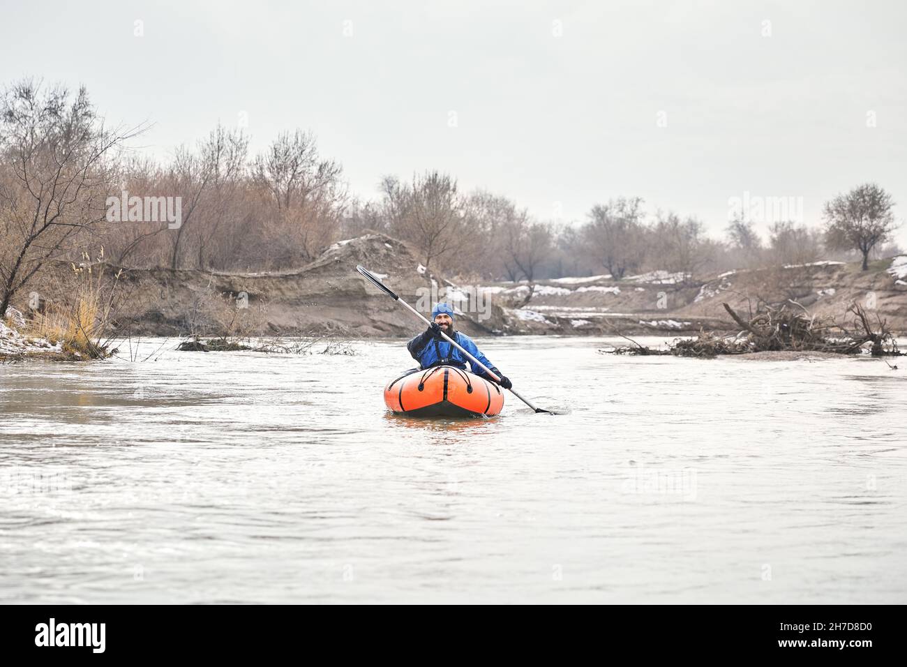 L'uomo è a pagaiare su una barca di zattera arancione nel fiume in inverno Foto Stock