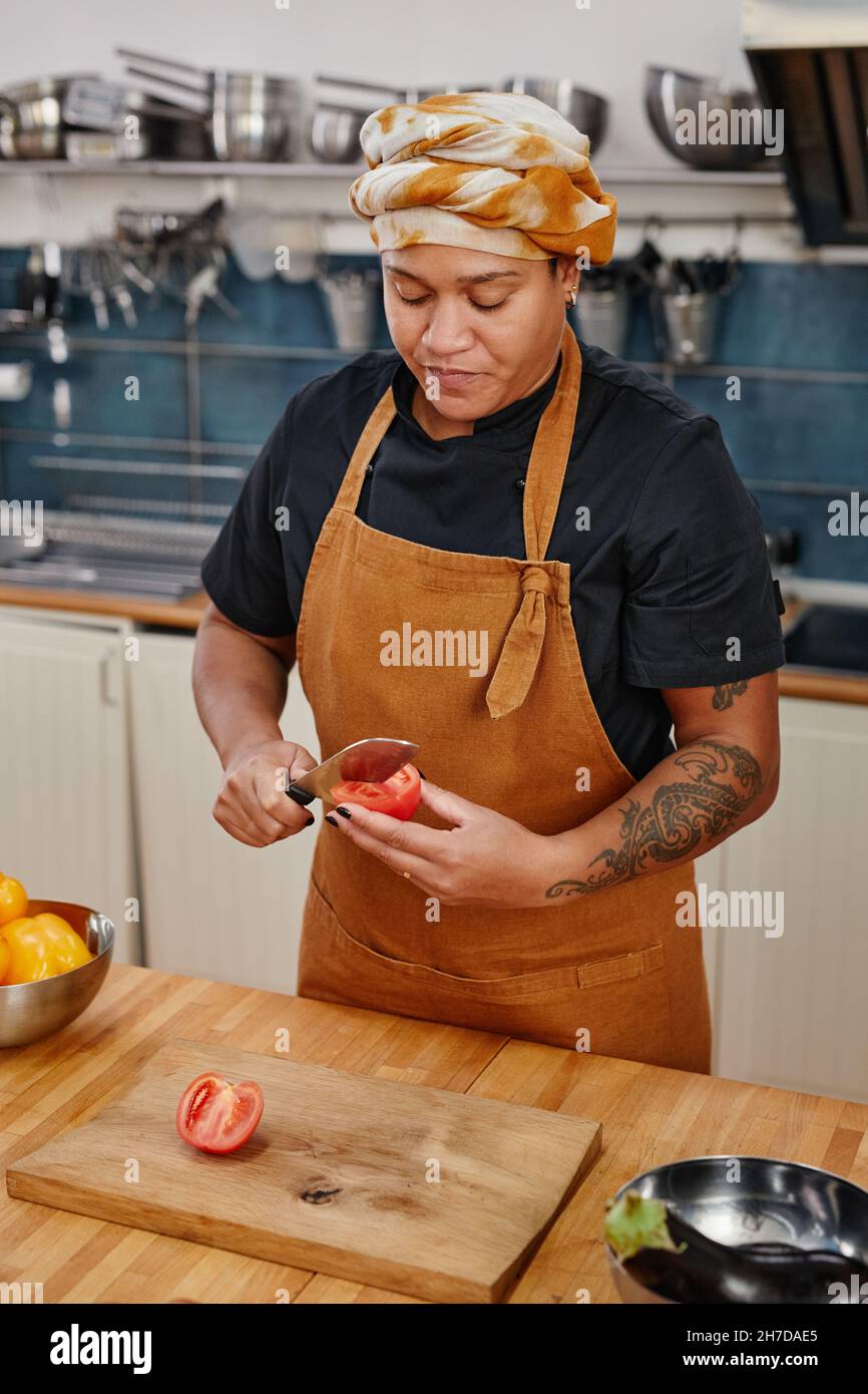 Ritratto verticale di donna tatuata che cucina verdure in cucina interno Foto Stock