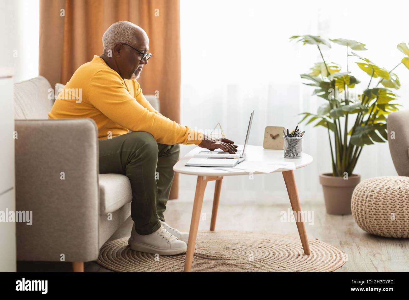 Senior African Man digitando su laptop Working Online a casa Foto Stock