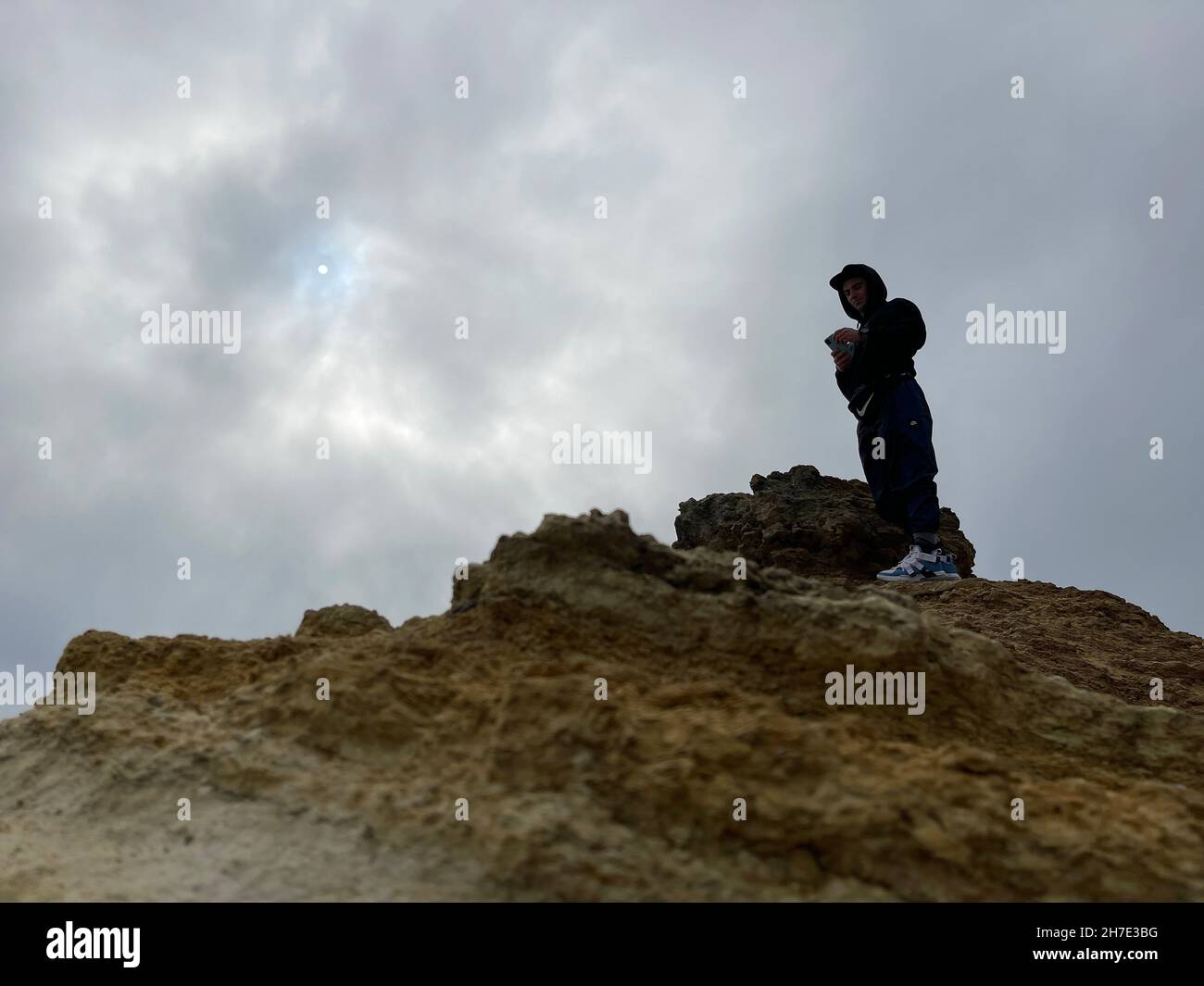 Scatto ad angolo basso di un arrampicatore sulla cima di una roccia gialla sotto il cielo grigio nuvoloso Foto Stock