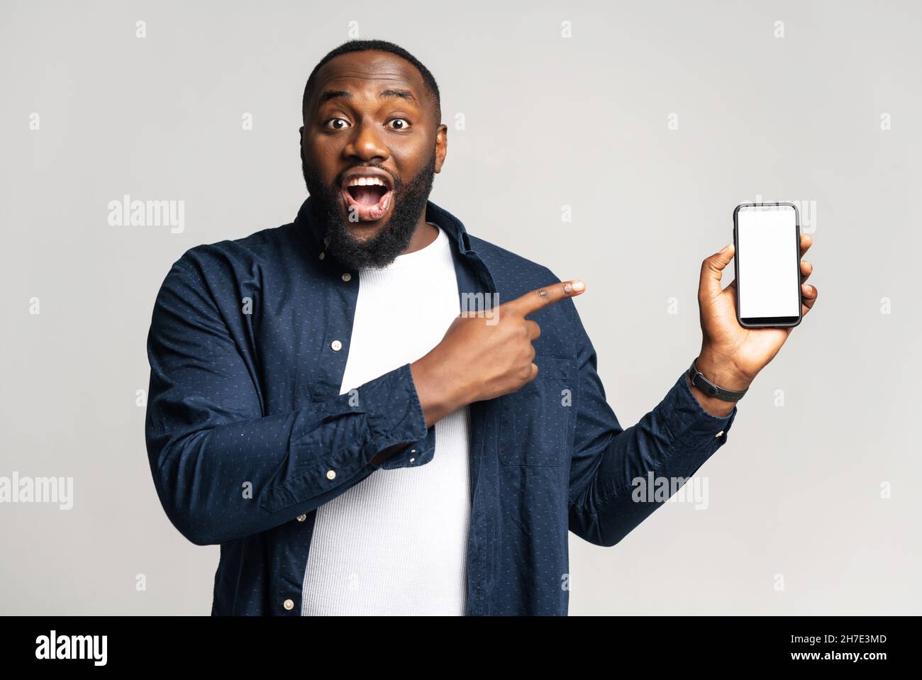 Domandato uomo afro-americano felice in camicia casual su t-shirt stand  isolati su bianco, punti indice dito su smartphone con schermo vuoto, nero  ragazzo stupito con affare, pubblicità nuova app Foto stock -