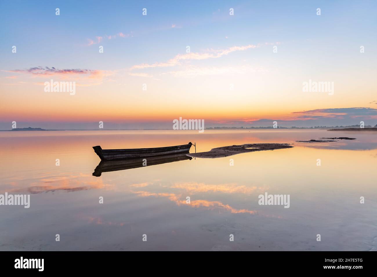 Incredibile alba. Barca solitaria nel lago tranquillo. La silhouette si riflette sull'acqua. Bella giornata estiva. Cielo blu con nuvole. Posizione posiziona gravità Foto Stock