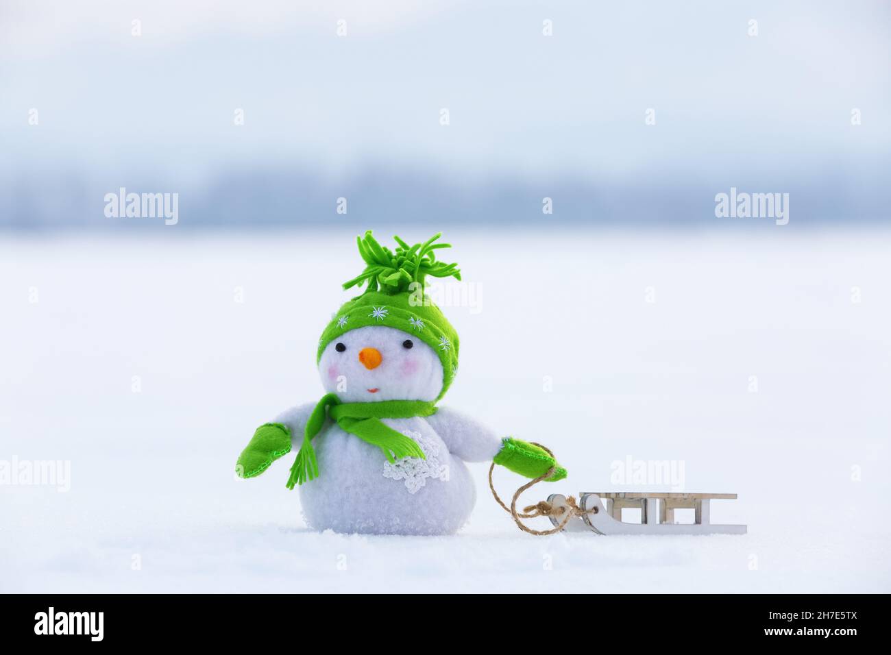 Snowman in cappello verde, guanti e sciarpa tira la slitta. Bellissima giornata invernale. Felice Anno Nuovo. Foto Stock