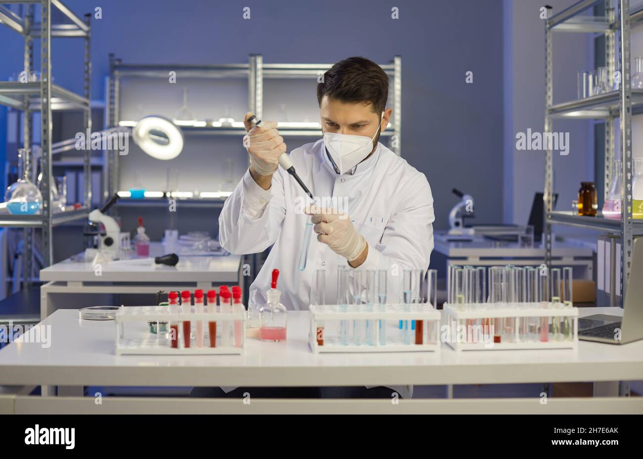 L'uomo attento e serio scienziato con pipetta aggiunge liquido alla provetta in laboratorio medico. Foto Stock