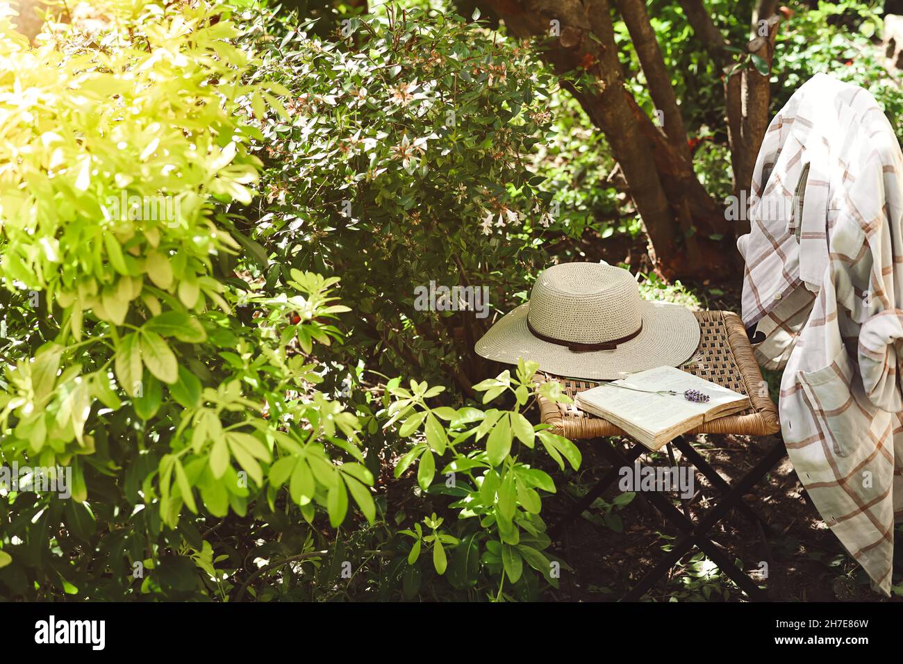 Un libro aperto e cappello estivo da donna su vecchia sedia in vimini in giardino, provenza e natura slow life concept Foto Stock