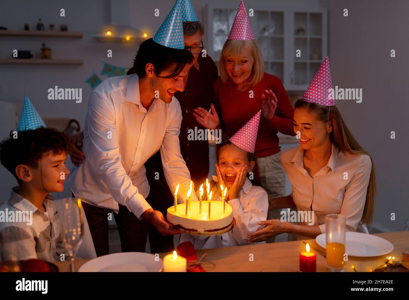 Adorabile bambina ottenere torta di compleanno con candele accese da famiglia amorevole, festeggiando la vacanza a casa in serata Foto Stock