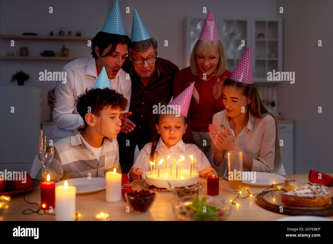 Carina bambina che soffia candele sulla torta di compleanno, facendo il desiderio, celebrando la vacanza con la sua grande famiglia amorevole a casa Foto Stock