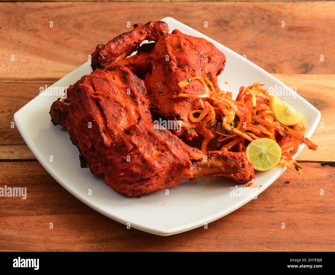 Pollo Tandoori - preparato arrostendo il pollo marinato nello yogurt e le spezie in un tandoor, servito su un fondo rustico in legno. Fuoco selettivo Foto Stock