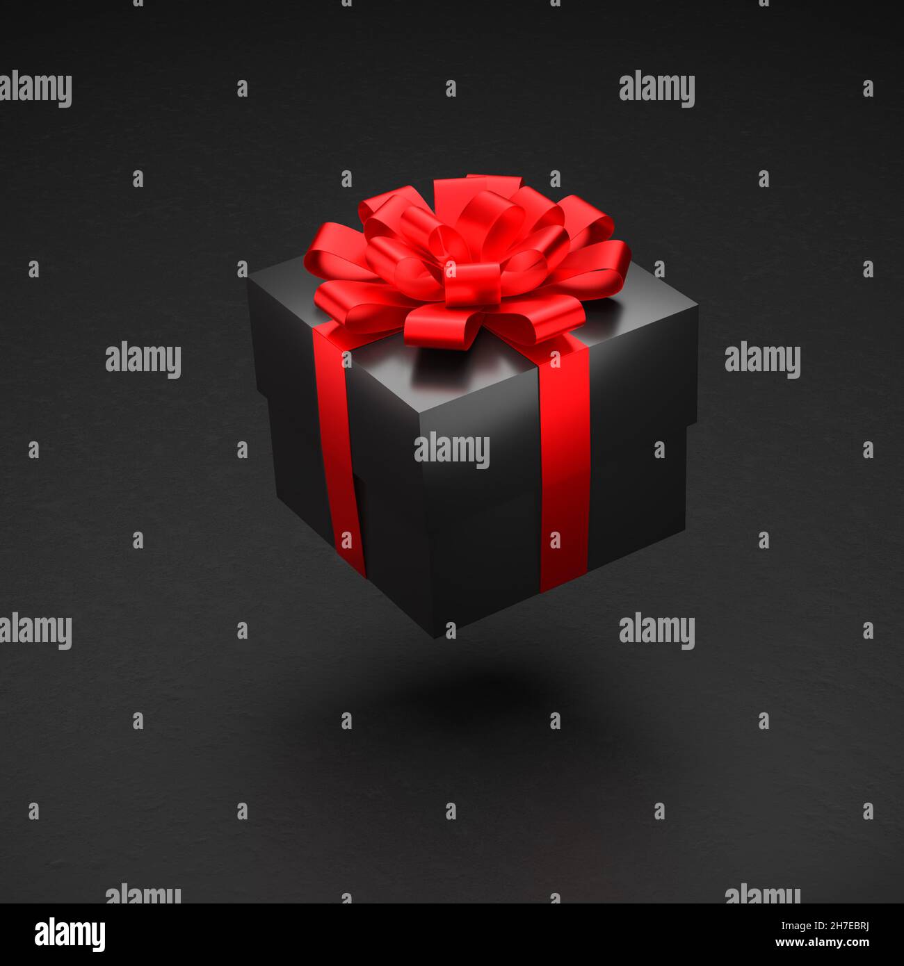 Una scatola regalo nera con nastro rosso e arco che si sorreggono su uno sfondo nero. Foto Stock