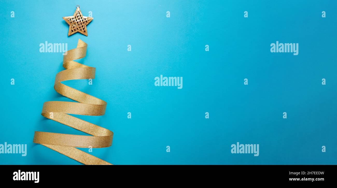 Nastro dorato a forma di albero di Natale su sfondo blu. Stella oro lucido sulla parte superiore. Buon Natale e felice anno nuovo modello di scheda di auguri Foto Stock