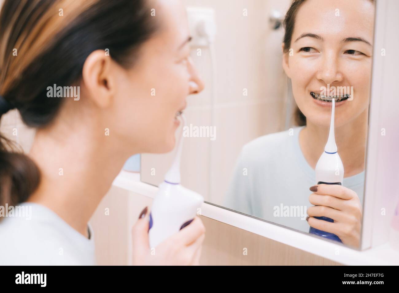 Donna con bretelle sui denti spazzolando i denti con utilizzando un irrigato, prima di specchio. Foto Stock
