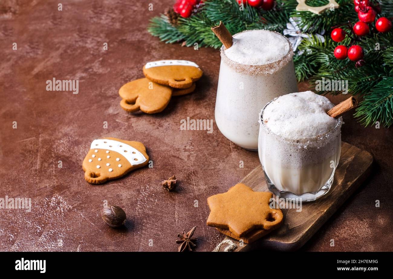 Punch all'uovo, liquore all'uovo con rami di albero di Natale, pan di zenzero e decorazioni su sfondo marrone. Eggnog bevanda di Natale in diversi bicchieri, selecti Foto Stock