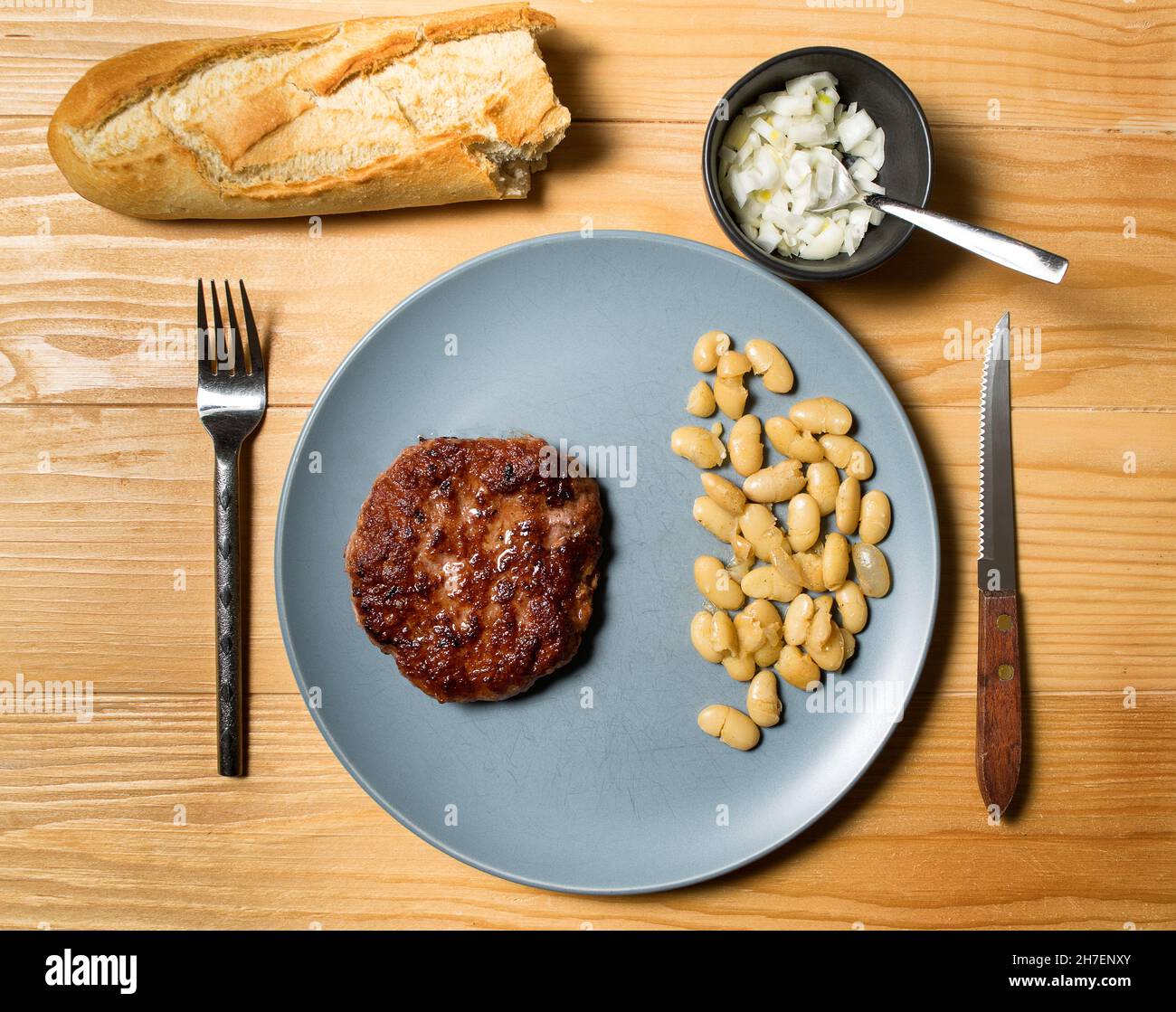 Gustoso hamburger alla griglia servito con fagioli vegetariani cotti in un piatto su un rustico tavolo di legno. Disposizione piatta, vista dall'alto Foto Stock