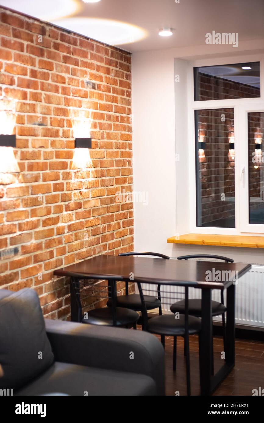Soggiorno interno in stile loft. Divano e tavolo da pranzo su un muro di mattoni sfondo con lampade. Foto Stock
