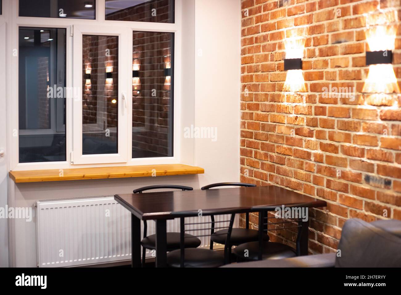 Soggiorno interno in stile loft. Divano e tavolo da pranzo su un muro di mattoni sfondo con lampade. Foto Stock