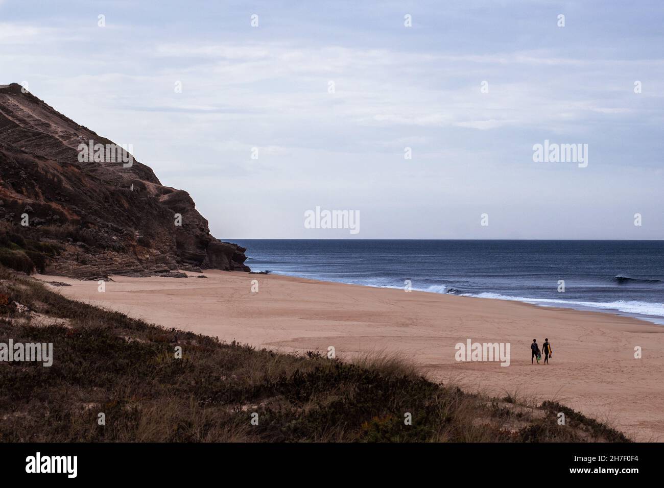 Paesaggio roccioso che incornicia un punto nascosto alla spiaggia di Quiaios con due persone in lontananza che navigano verso l'oceano Atlantico. Destinazione Surfers' Foto Stock