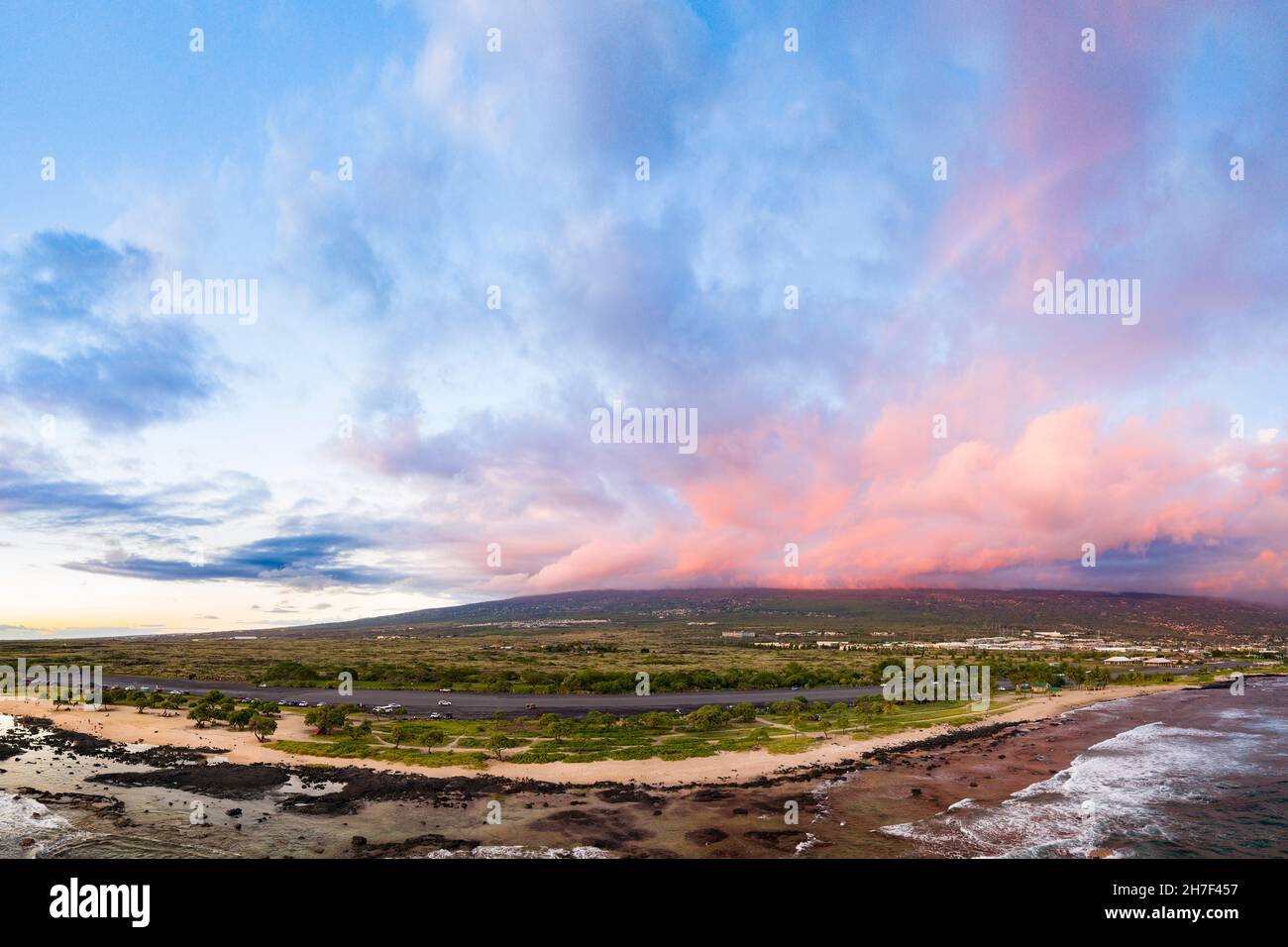 Un debole arcobaleno si forma mentre il sole che tramonta illumina le nuvole rosa sulle pendici del Vulcano Hualalai, come si vede dall'Old Kona Airport County Park, Hawaii Foto Stock