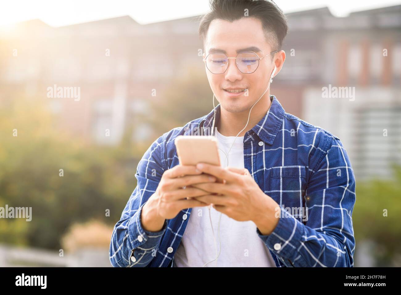 sorridendo giovane asiatico ascoltando musica e utilizzando il telefono cellulare mentre si cammina Foto Stock