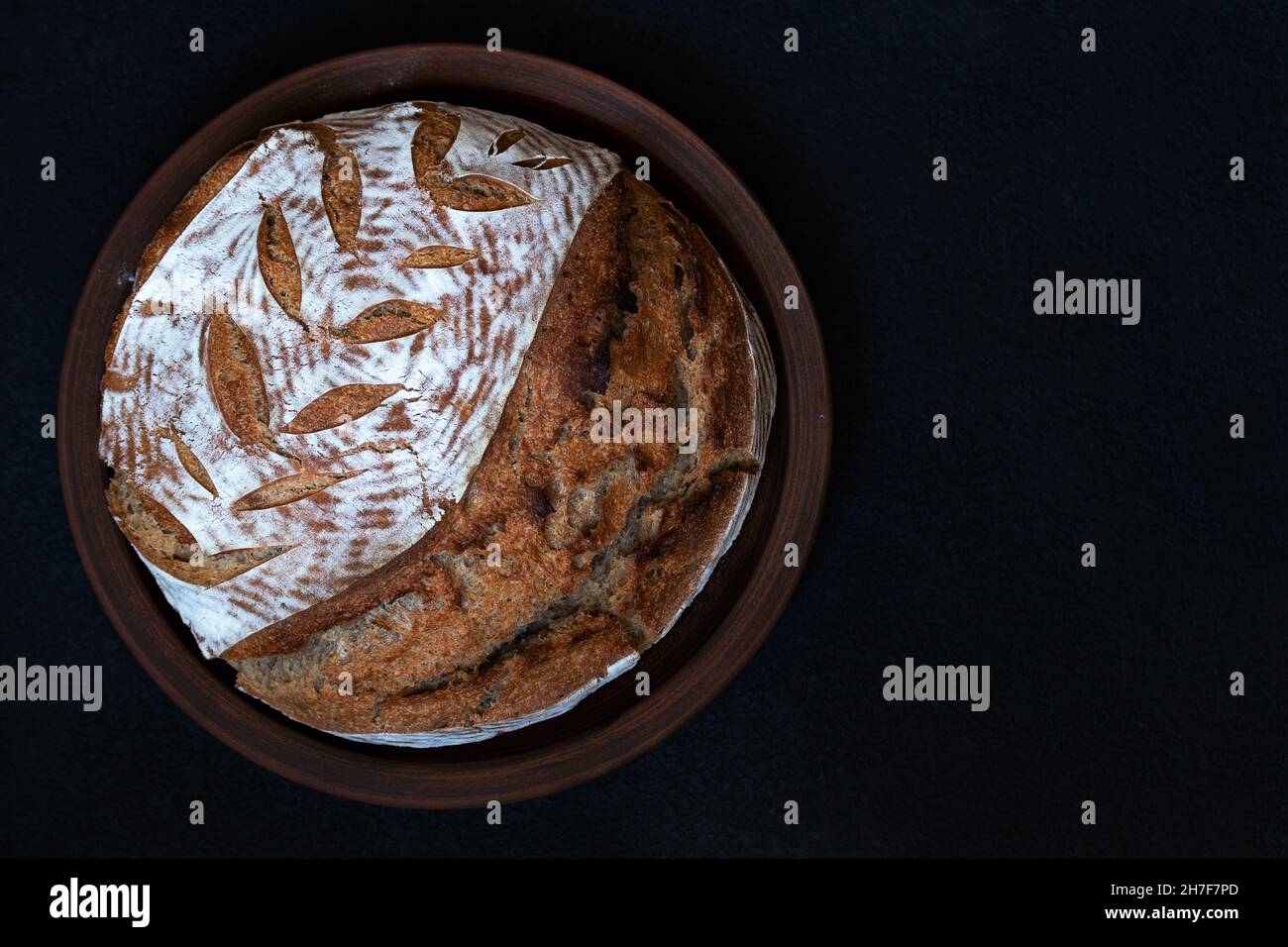 Pane scuro rotondo fatto in casa con crosta di farina e spikelet dipinto su un piatto di argilla. Vista dall'alto con spazio di copia. Foto Stock