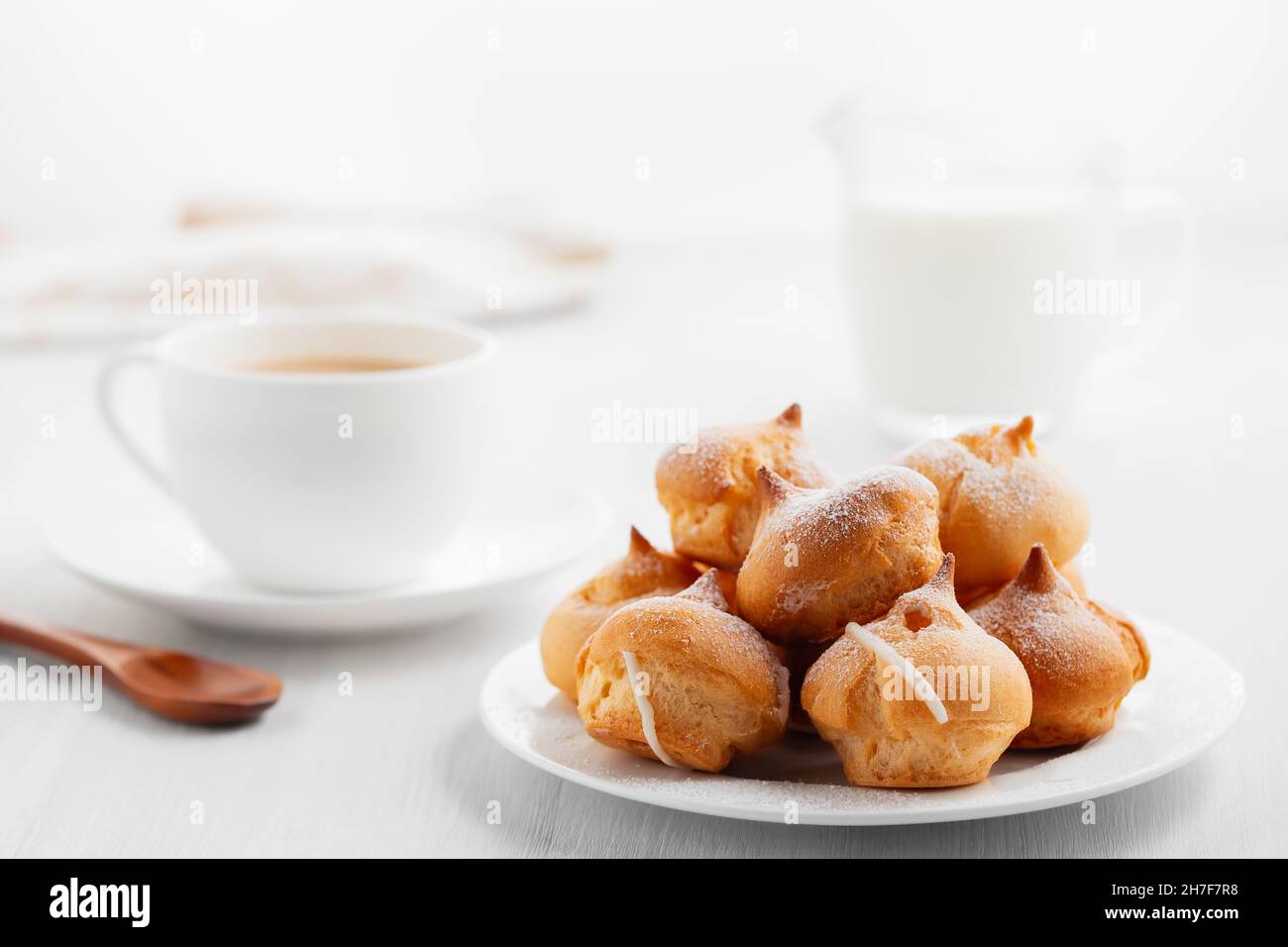 Caffè del mattino con torte. Profiteroles, caffè, crema su un tavolo di legno bianco Foto Stock