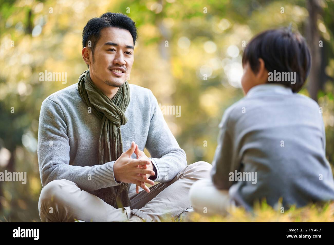 padre e figlio asiatici seduti sull'erba per una piacevole conversazione all'aperto nel parco Foto Stock