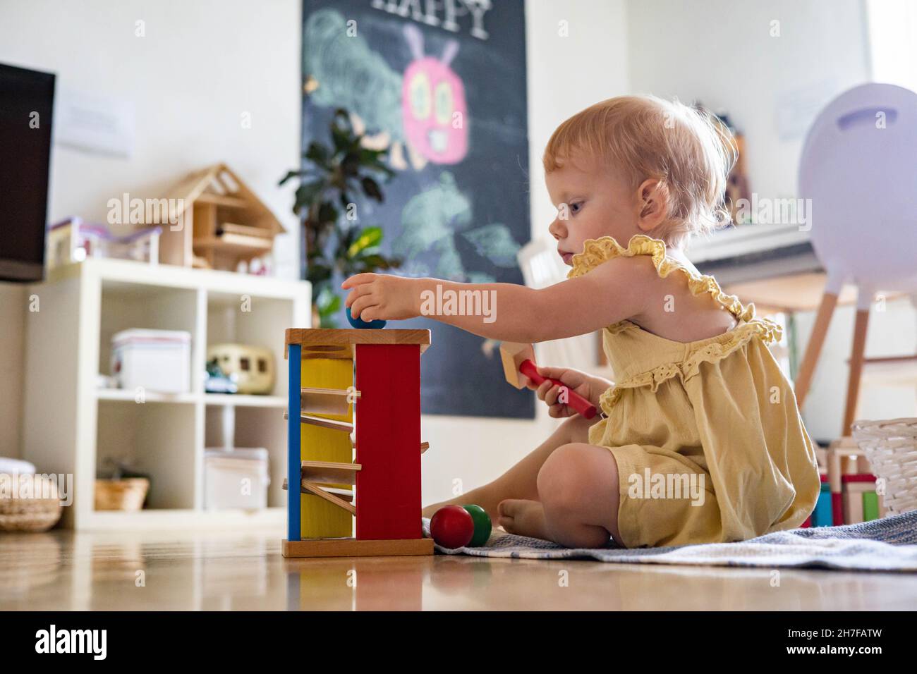 Bambino felice ragazza che colpisce martello di legno su palline colorate giocattolo ecologico di sviluppo precoce Foto Stock