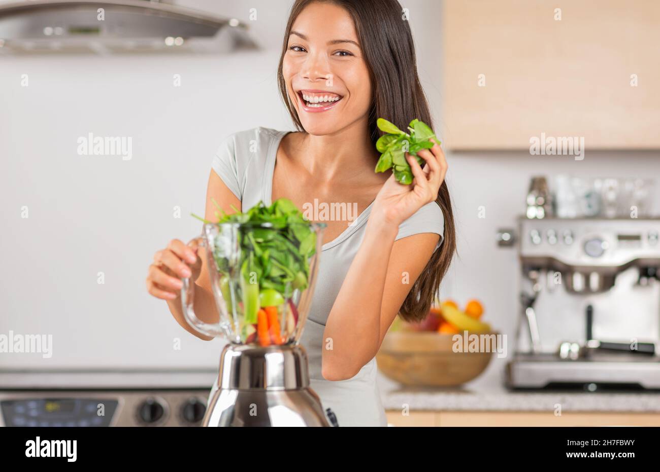 Frullato verde sano donna asiatica usando gli spinaci nel frullatore per fare disintossicare il succo vegetale a casa. Giovane donna sorridente che cucinava Foto Stock