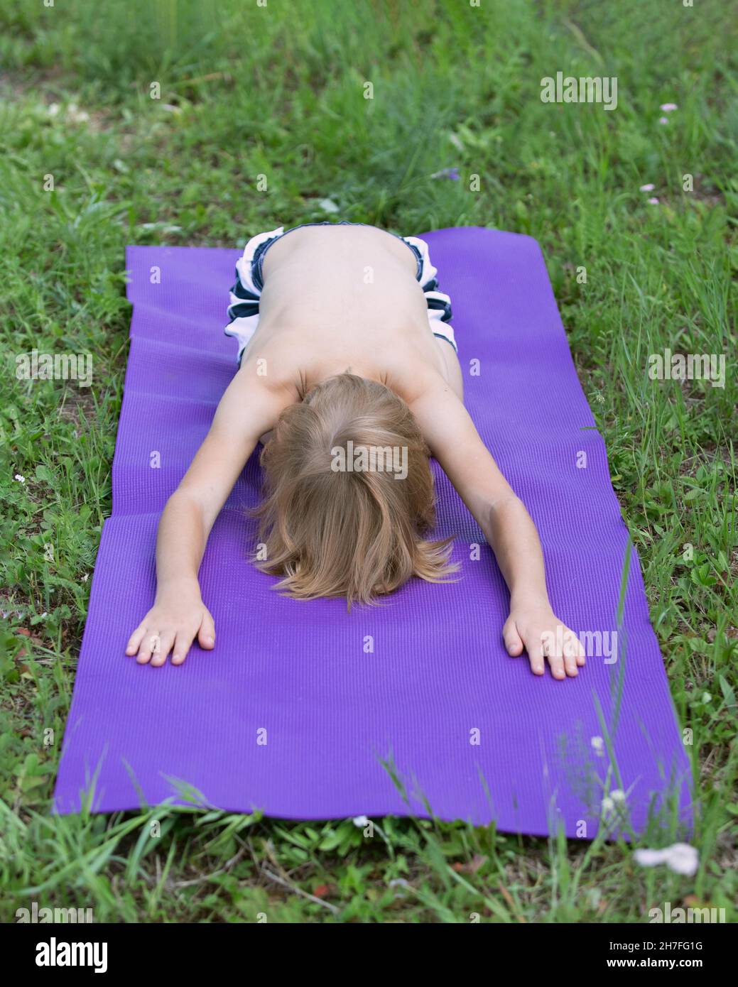 Il bambino piccolo caucasico fa yoga, posizione lepre nel parco all'aperto. Shashankasana Kids Yoga Foto Stock