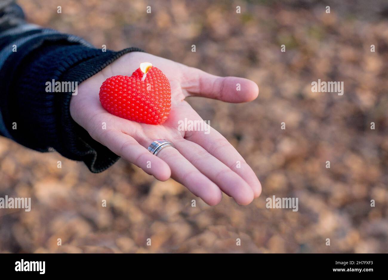 Fuoco selettivo di una mano che tiene una candela a forma di cuore Foto Stock