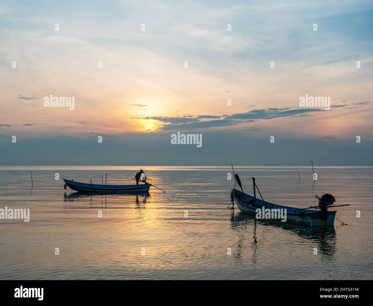 Uomo che prepara la sua barca all'alba sulla costa della provincia di Surat Thani in Thailandia. Foto Stock