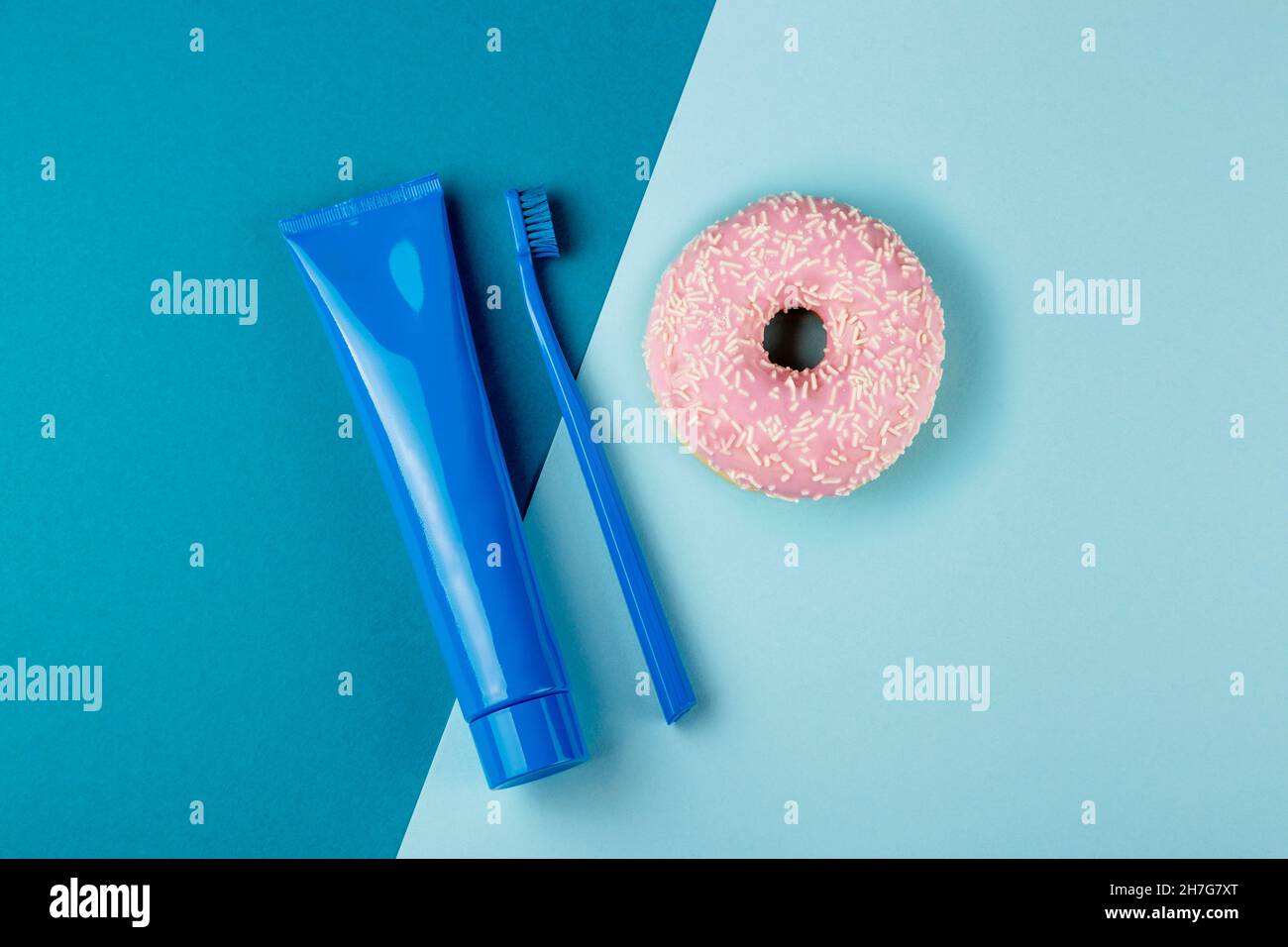 Tubo blu di dentifricio spazzolino blu e ciambella rosa giacciono su sfondo blu combinato. Vista dall'alto Foto Stock