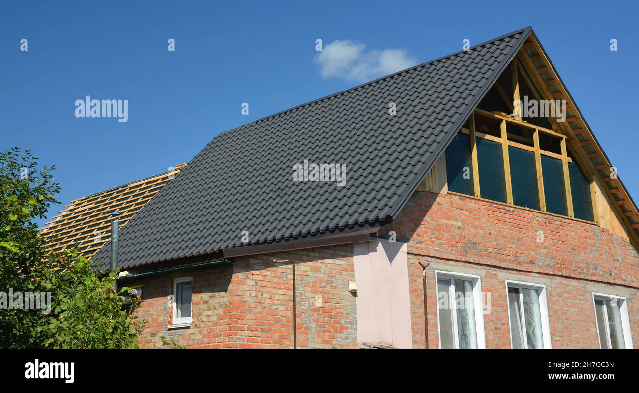 Costruzione di tetti. Una ristrutturazione di casa in mattoni con un tetto a timpano riparazione sul palco di incorniciatura tetto, tegole di metallo tetto e l'installazione di finestre soffitta. Foto Stock