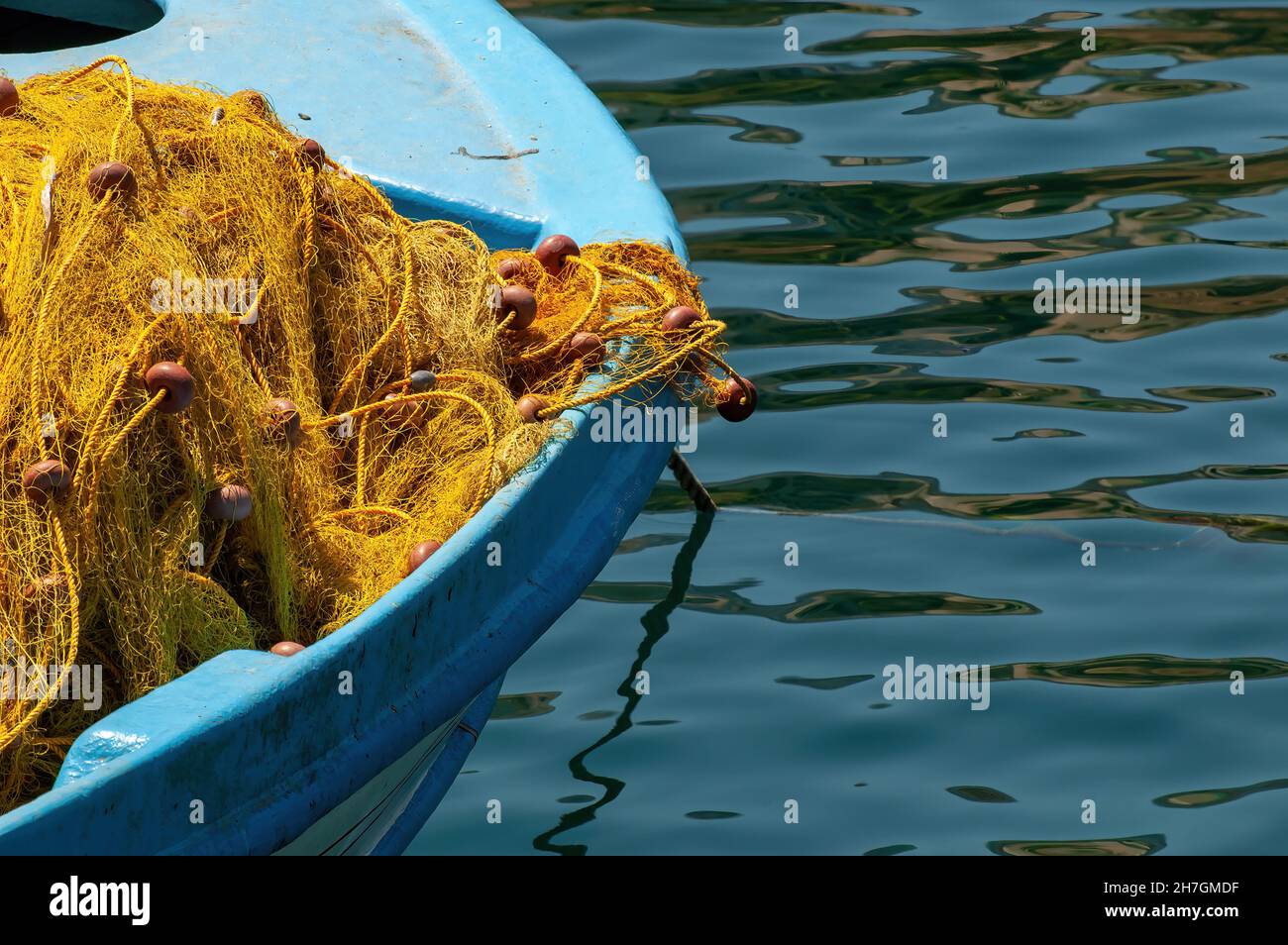 Vista ravvicinata della parte anteriore di una barca da pesca di legno blu ormeggiata con reti da pesca di nylon giallo con corda e galleggianti drappeggiati sulla parte anteriore della barca Foto Stock