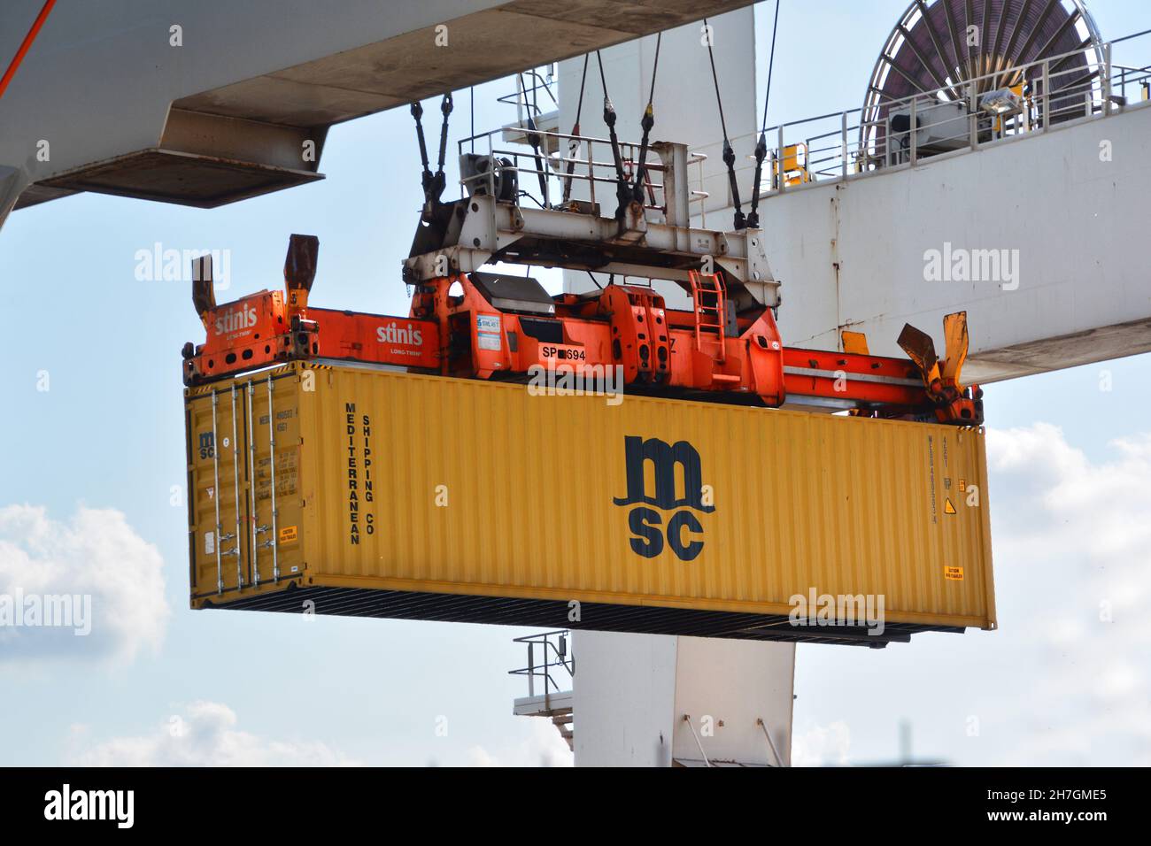 Rotterdam, Paesi Bassi-Aprile 2020: Vista ravvicinata da una gru a portale verso un container marino giallo chiaro sollevato da uno spanditore per ulteriori Foto Stock