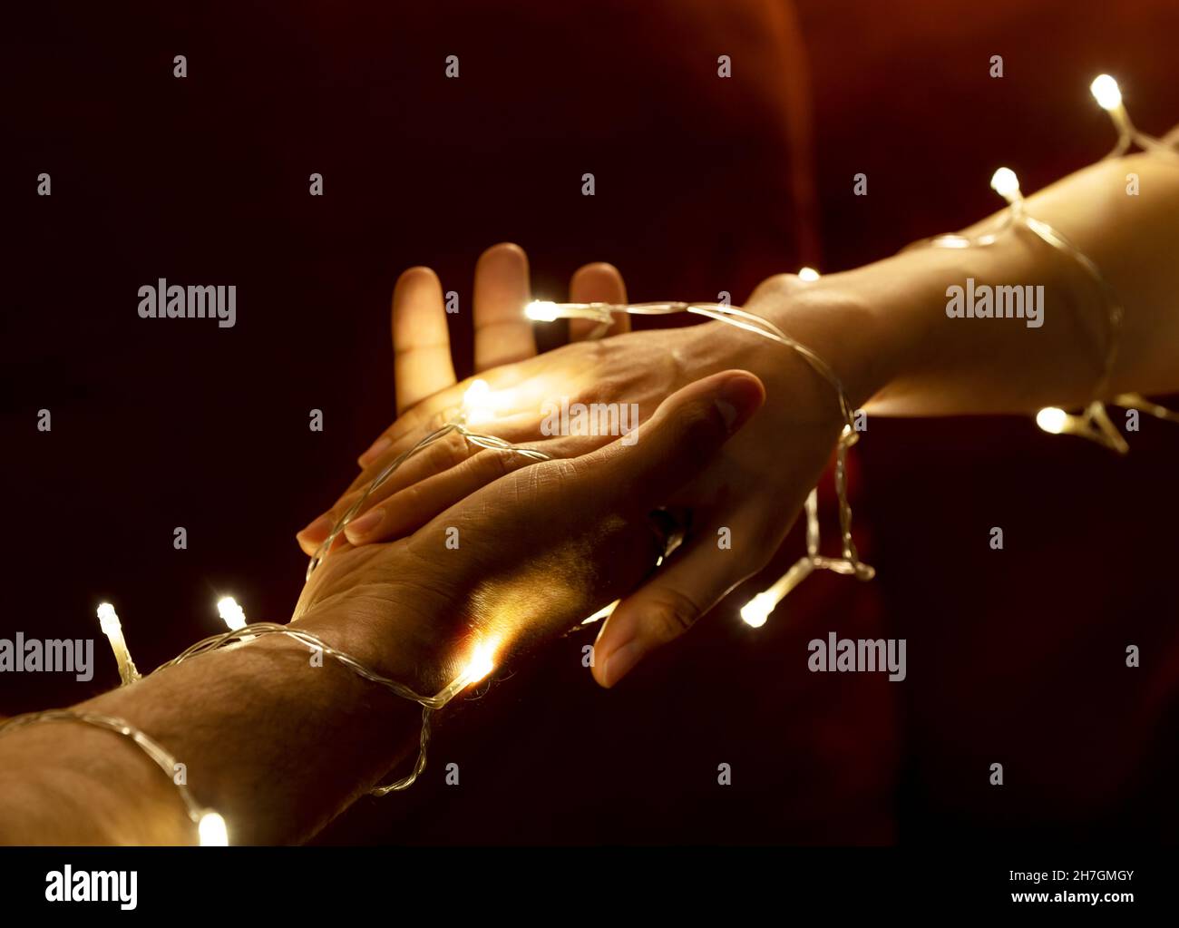 Coppia tenendo le mani l'un l'altra come mani coperte con luci a LED. Datazione e concetto di amore. Foto Stock