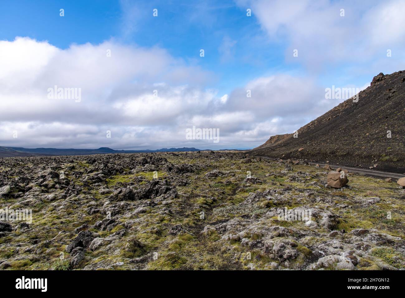 Vista ad angolo basso del paesaggio arido di roccia lavica nera, alcune ricoperte di muschio, dal vicino vulcano Katla sull'Islanda con montagne sul retro Foto Stock
