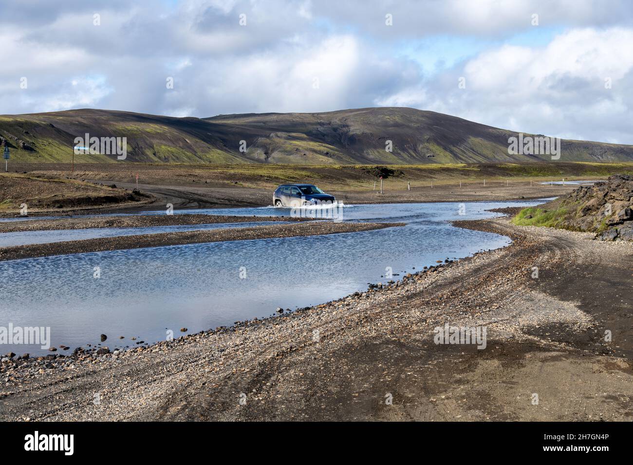 Vista di un'auto a quattro ruote motrici nell'acqua di un fiume in uno degli incroci vicino vulcano Katla su Islanda con montagne sullo sfondo con l Foto Stock
