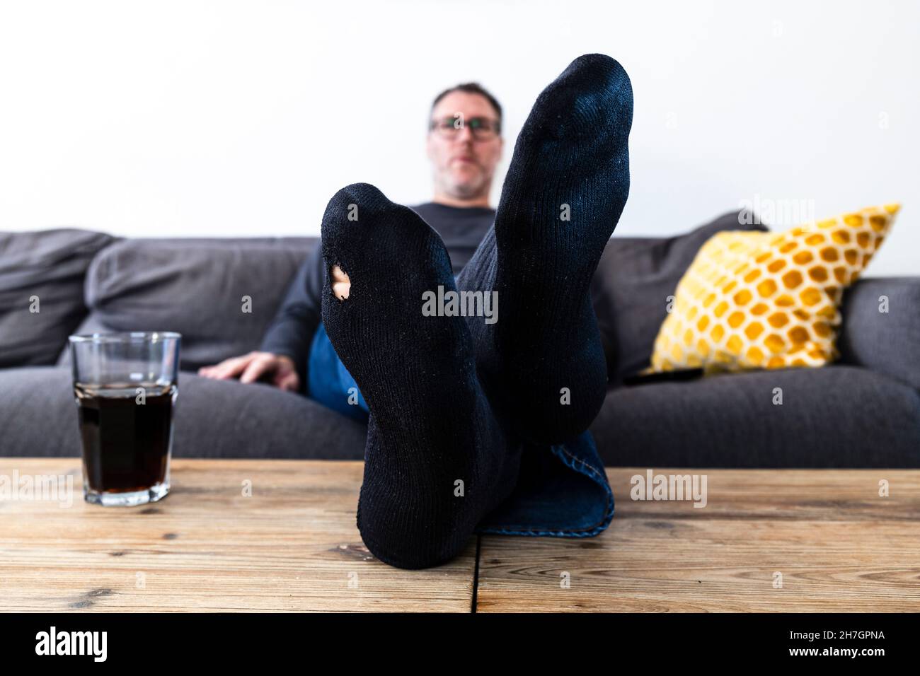 Uomo con un buco nel calzino seduto sul divano Foto Stock