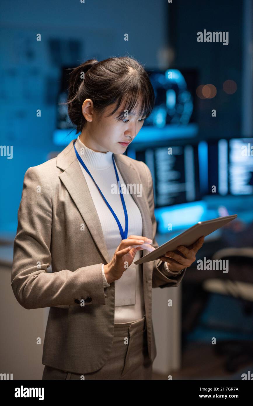 Giovane donna d'affari asiatica in formalwear che scorre in tablet mentre cerca in rete nuovi metodi di decodifica dei dati digitali Foto Stock