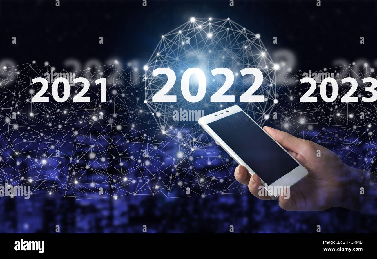 Anno di carico dal 2021 al 2022. Start Concept.Hand tenere smartphone bianco con ologramma digitale 2022 segno sulla città scuro sfondo sfocato. Concetto per visio Foto Stock