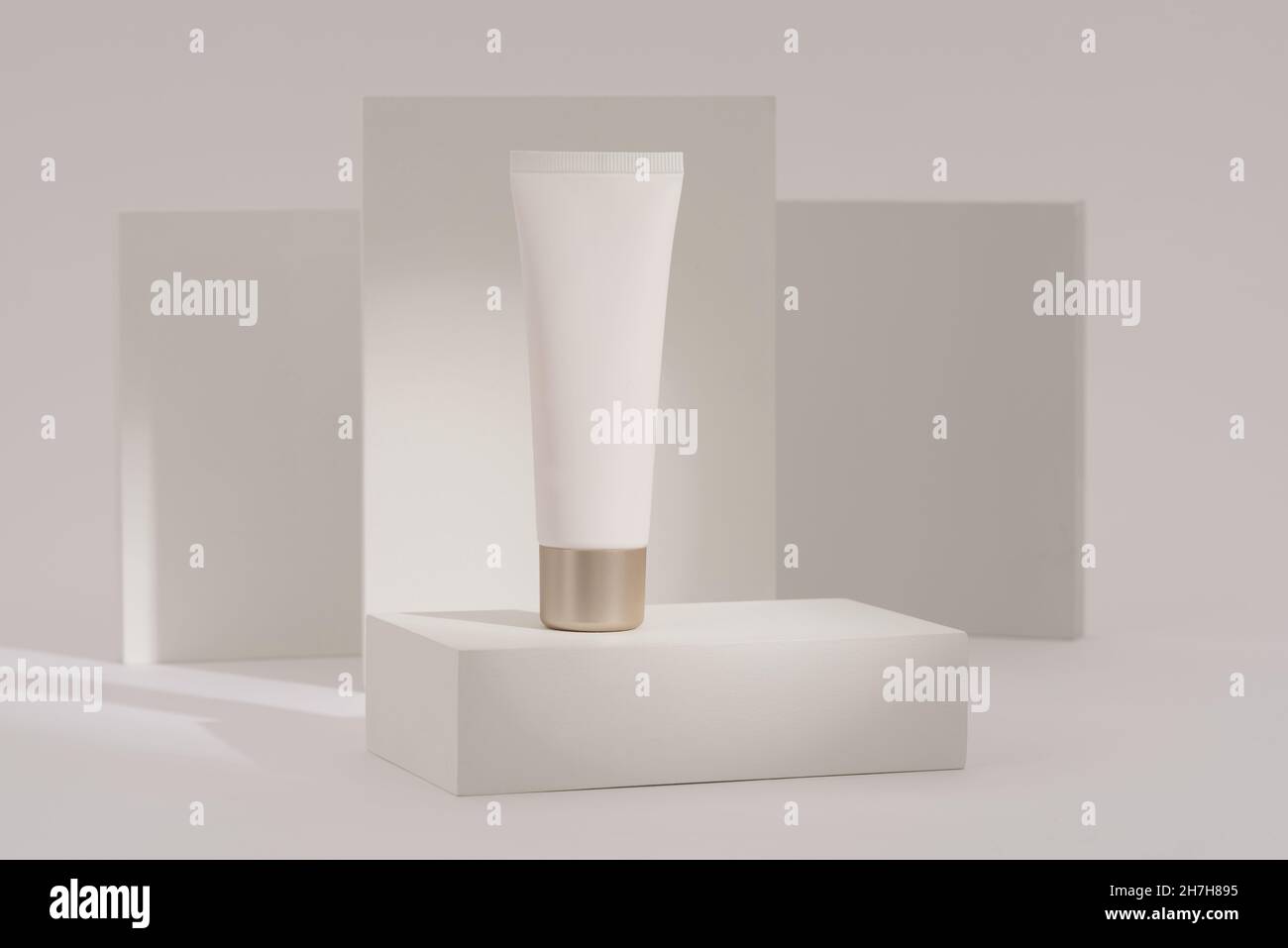tubo bianco di crema per la cura della pelle o prodotto cosmetico contro uno sfondo bianco minimalista con dettagli ombreggiati Foto Stock