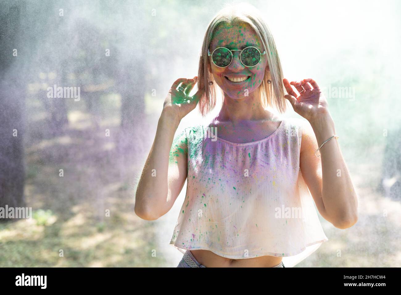Ragazza felice con vernici a polvere sul viso celebrando il festival del colore Holi. Ritratto di una giovane donna nel parco a Colorfest. Concetto di festa Holi Foto Stock