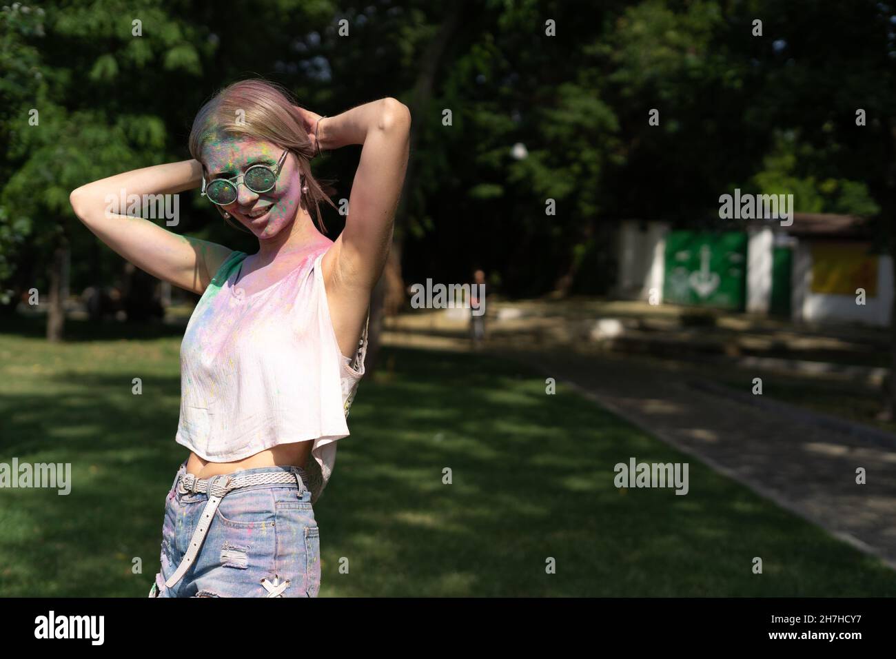 Festival dei colori Holi. Ritratto di una ragazza bella e felice al festival Holi. Ragazza bionda nel parco con un volto sporco. Vernice a polvere colorata Foto Stock