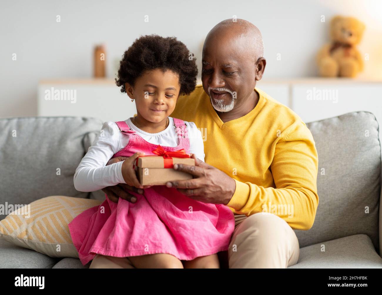 Sorridendo maschio di età nera dà il regalo di compleanno alla bambina in soggiorno Foto Stock