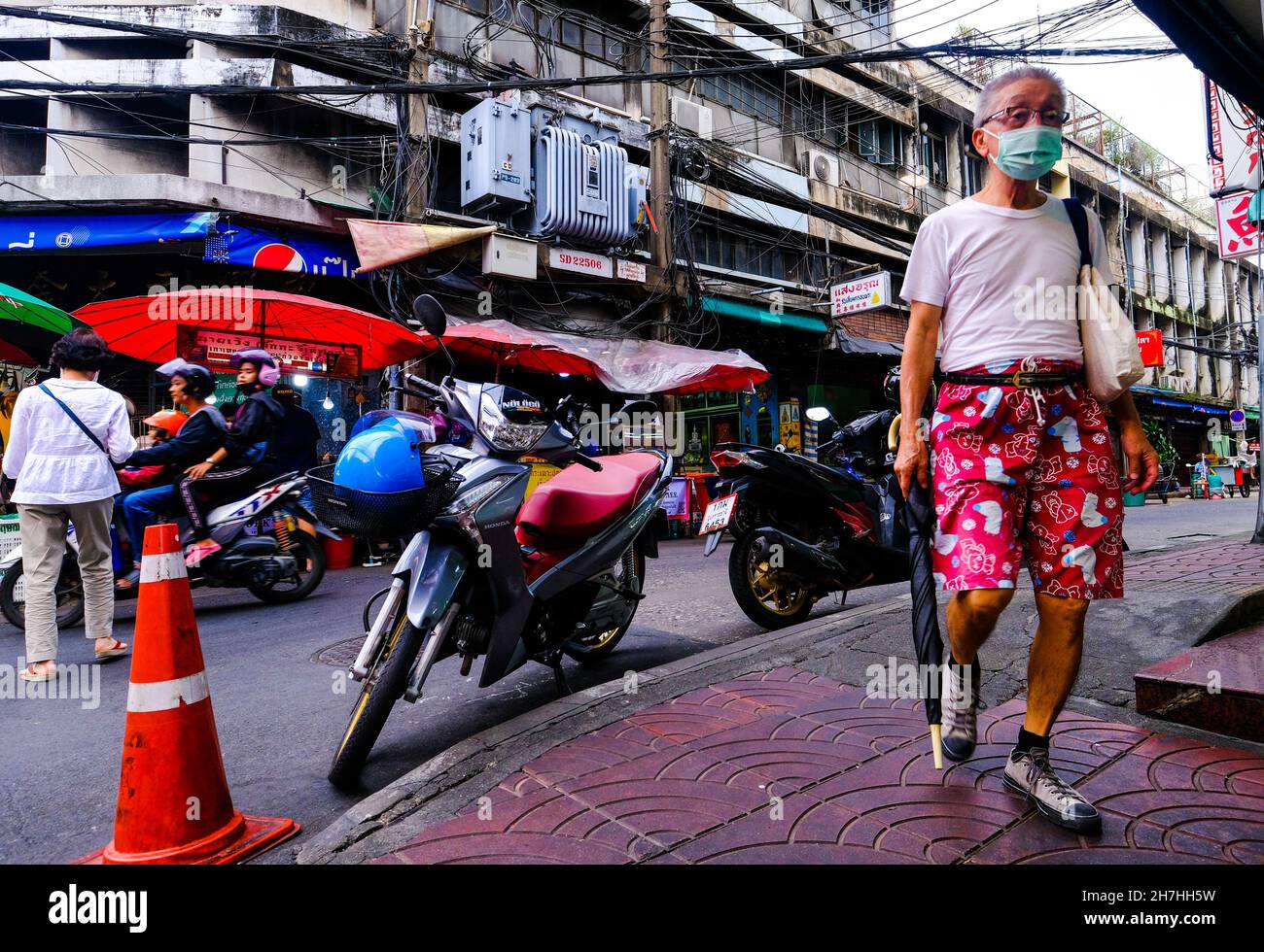 Un uomo anziano che indossa pantaloncini colorati cammina lungo il marciapiede a Chinatown, Bangkok Thailandia Foto Stock