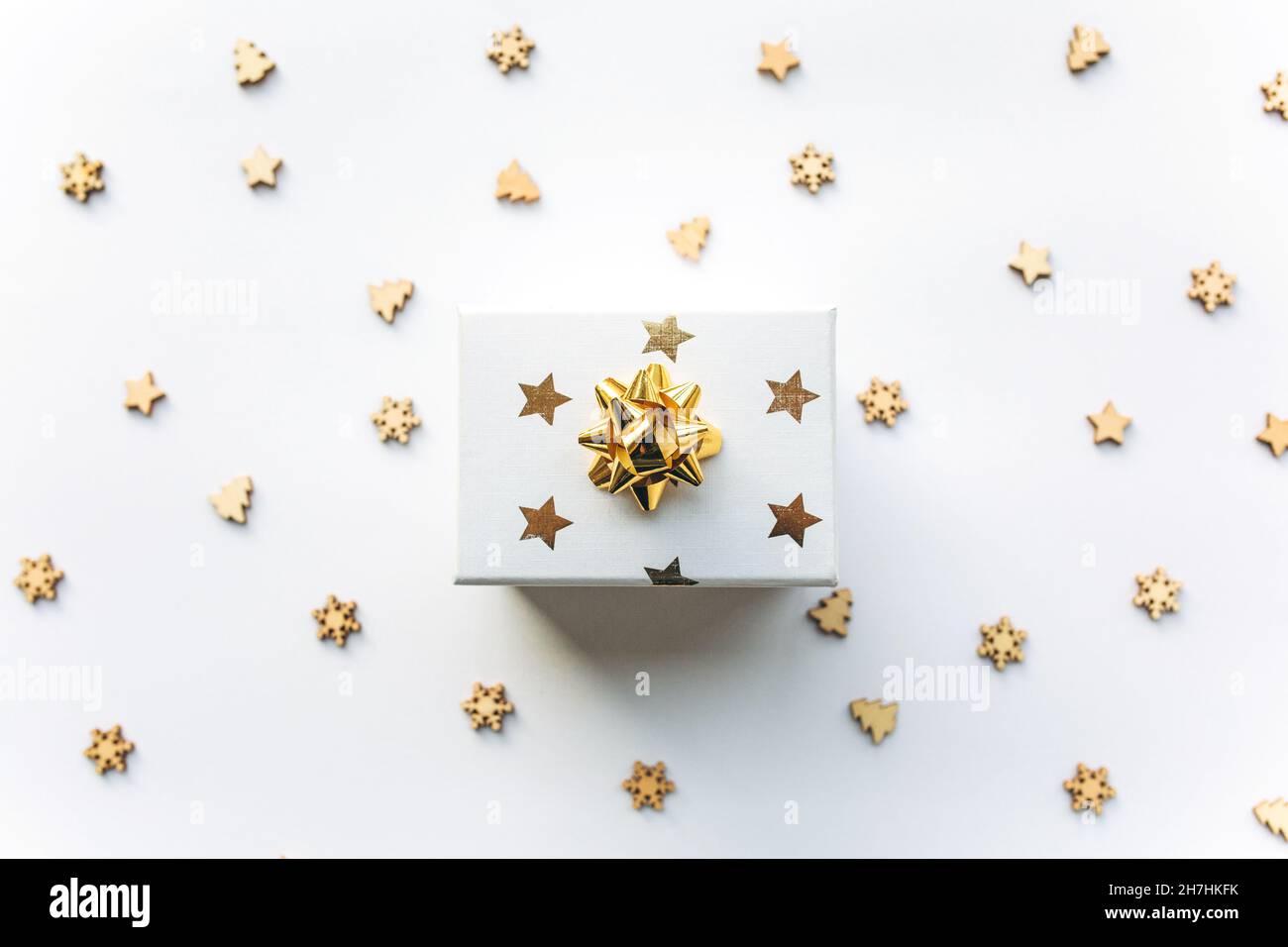 Confezione regalo bianca con nastro d'oro con tinsel e confetti natalizi in legno su sfondo bianco. Concetto regalo, anno nuovo, sfondo festivo. Disposizione piatta, vista dall'alto Foto Stock